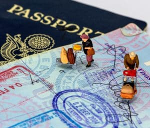 Pequeñas figuras de viajeros caminan con su equipaje sobre la página de visado de un pasaporte, simbolizando el trámite para solicitar el Modelo 149 Ley Beckham como expatriado en España.