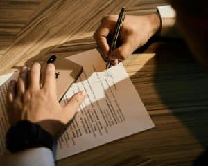Persona firmando un documento sobre una mesa de madera mientras repasa los requisitos para desheredar en España.
